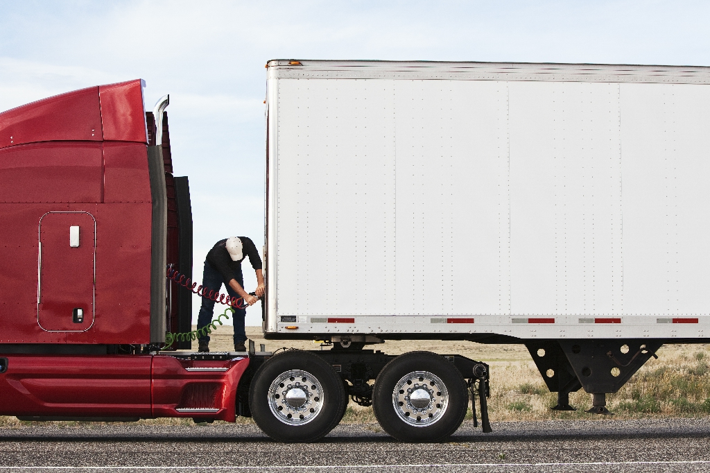 View of a driver connectiing the power cables to trailer of a  commercial truck.